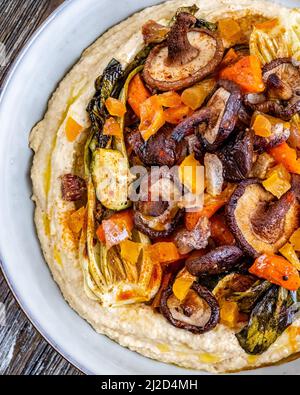 Gros plan de houmous avec légumes rôtis dans une assiette blanche sur une table en bois Banque D'Images