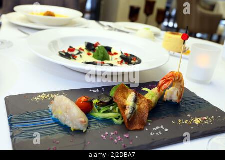 Assiette de fruits de mer mélangés derrière les raviolis d'encre de calaques noires sur la table du restaurant. Banque D'Images