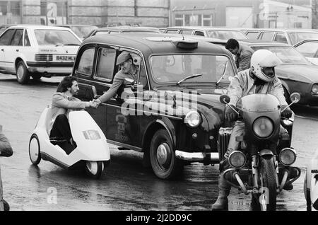 La photo du nouveau véhicule électrique montre un monsieur à Londres au volant du Sinclair C5, conçu par Sir Clive Sinclair. Ici, il rencontre un chauffeur de taxi, et à proximité est une moto. Le taxi et la moto typiques du type de circulation de la C5 se mélangent avec sur les routes très fréquentées de Londres. Photo prise le 10th janvier 1985 Banque D'Images