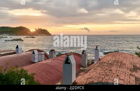 Coucher de soleil depuis les toits de cheminées des maisons de pêcheurs sur la plage de Cala Margarida à Palamos, Costa Brava. Banque D'Images