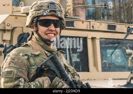 Soldat souriant du corps des Marines des États-Unis avec des lunettes de soleil, un fusil de chasse et un véhicule blindé humvee en arrière-plan pendant la guerre, les troupes des États-Unis ou de l'armée américaine Banque D'Images