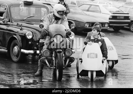 La photo du nouveau véhicule électrique montre un monsieur à Londres au volant du Sinclair C5, conçu par Sir Clive Sinclair. Ici il rencontre une moto et un pilote, et tout près il y a un taxi. Le taxi et la moto typiques du type de circulation de la C5 se mélangent avec sur les routes très fréquentées de Londres. Photo prise le 10th janvier 1985 Banque D'Images