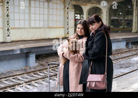 Maman et fille se sont rencontrées joyeusement sur la plate-forme et embrasser, dans les mains petit chien, il y a une grande valise sur le sol en hiver la saison neigeuse. Relation dans la famille Banque D'Images