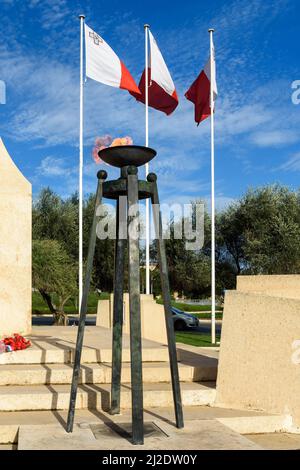 Floriana, Malte - novembre 26th 2018 : l'une des flammes éternelles au Mémorial de la guerre de Floriana, derrière elle se trouvent trois drapeaux nationaux maltais. Banque D'Images