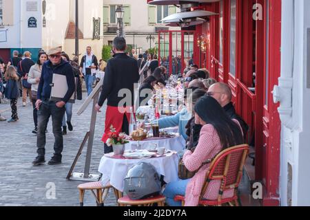 Paris, France - 22 mars 2022 : touristes dînant à l'extérieur dans le quartier pittoresque de Montmartre et servis par un serveur français Banque D'Images