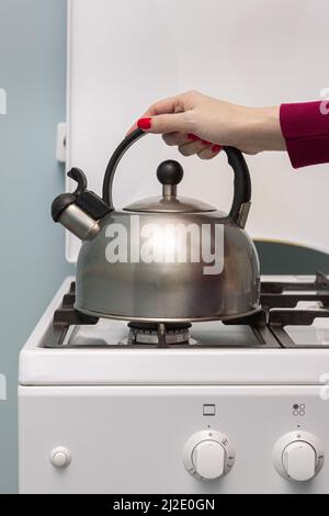 une main femelle place une bouilloire métallique sur un brûleur à gaz. Photo de haute qualité Banque D'Images