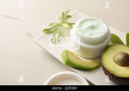 Crème hydratante naturelle avec extrait d'avocat pour le soin de la peau avec des fruits et des feuilles plaque sur table blanche. Composition horizontale. Vue en hauteur. Banque D'Images