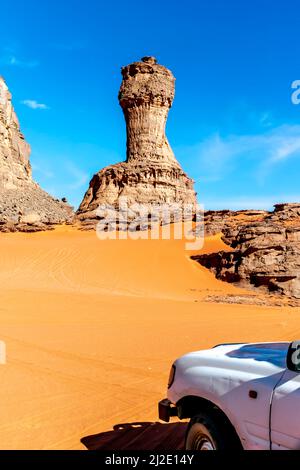 Coupe du monde en pierre de forme naturelle et partie avant du véhicule 4x4. Désert du Sahara de Tadrar Rouge, Djanet, Algérie. voiture 4WD qui regarde Rocky Mountain. Banque D'Images