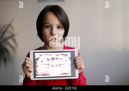 Enfant, portant des bretelles, préadolescent, tenant un comprimé avec une photo de ses dents de rayons X du dentisde lui à la maison Banque D'Images