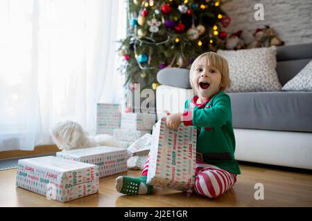 Joyeux enfant, tout-petit garçon, ouvre des cadeaux le jour de noël vêtus de pyjamas Banque D'Images