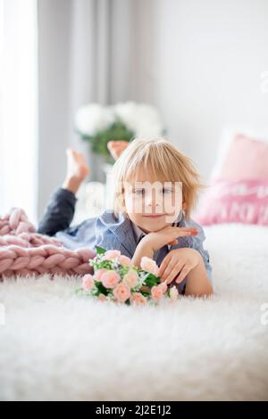 Mignon enfant blond avec chemise, assis sur le lit avec décoration de Saint-Valentin, arrière-plan isolé Banque D'Images