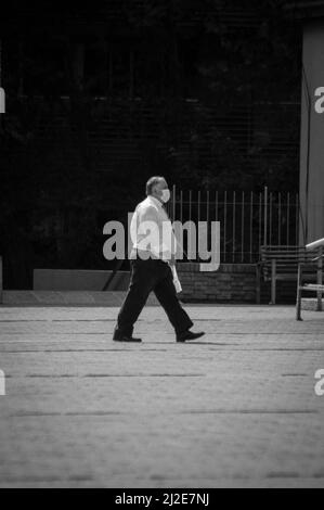 Un cliché vertical distant d'un homme âgé marchant dans la rue avec un masque médical en noir et blanc Banque D'Images