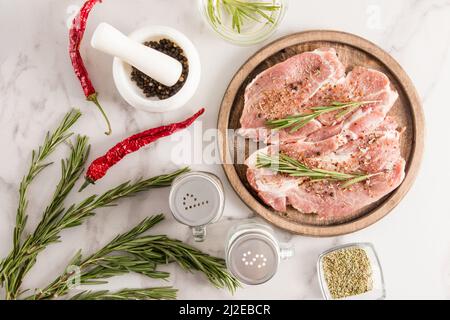 deux steaks de porc crus sur un plateau rond en bois et une table en marbre blanc prête à être grillée. délicieux aliments sains