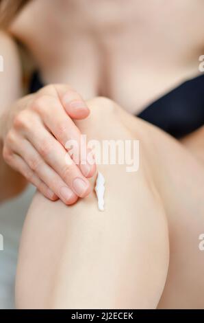 Une femme applique un hydratant sur la jambe, gros plan. Prendre soin de la peau des pieds. Banque D'Images