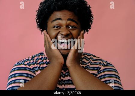 jeune homme afro-américain heureux posant dans le studio sur fond rose modèle masculin Banque D'Images