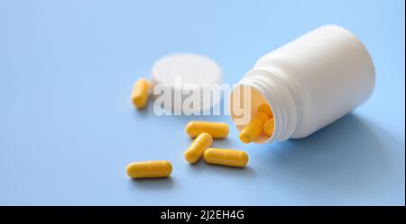 Capsules jaunes dispersées dans un contenant à médicaments en plastique blanc Banque D'Images