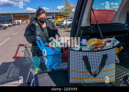 Femme déchargeant sa boutique hebdomadaire du tramway dans un parking de supermarché à l'arrière de sa voiture. NB : version du modèle disponible pour les personnes en premier plan Banque D'Images