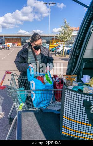 Femme déchargeant sa boutique hebdomadaire du tramway dans un parking de supermarché à l'arrière de sa voiture. NB : version du modèle disponible pour les personnes en premier plan Banque D'Images