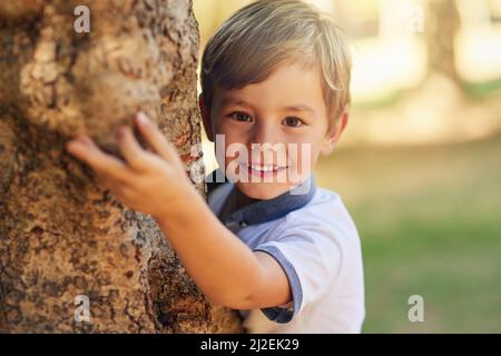 Masquer et rechercher un expert de niveau. Photo d'un petit garçon heureux jouant à côté d'un arbre dans le parc. Banque D'Images