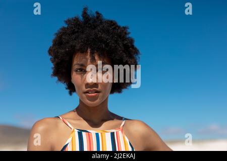 Portrait d'une jeune femme afro-américaine confiante avec une coiffure afro-américaine contre le ciel bleu Banque D'Images