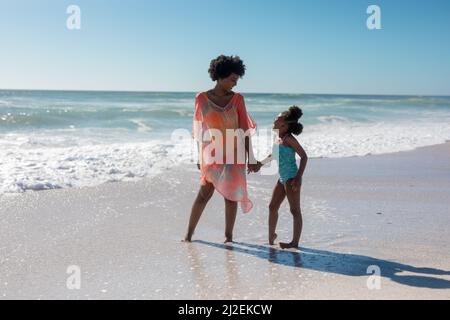 Mère et fille afro-américaines tenant la main tout en regardant l'une l'autre debout à la plage Banque D'Images