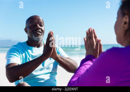 Afro-américain senior homme et femme avec les mains classed pratiquant le yoga à la plage Banque D'Images