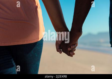 Section médiane d'un couple senior afro-américain tenant les mains à la plage Banque D'Images