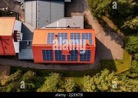 Vue aérienne au-dessus des panneaux solaires sur un toit de bâtiment rouge - de haut en bas, tir de drone Banque D'Images