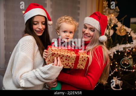 Une mère et une grande sœur donnent un cadeau à un enfant de deux ans à Noël. Banque D'Images