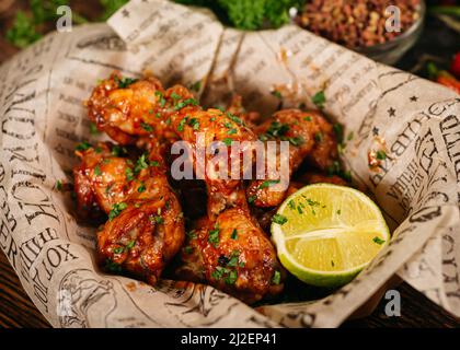 Portion de pilons de poulet frits en profondeur et couverts de sauce chaude (assaisonnée). Servi avec une moitié de lime sur papier artisanal. Banque D'Images