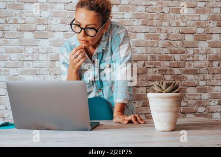 Les gens d'affaires en ligne style de vie et concept de travail moderne. Femme debout devant l'ordinateur regardant avec des doutes et l'expression réfléchie. Stock cryp Banque D'Images