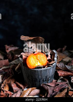 injection verticale d'oranges sanguines dans un seau en bois sur des feuilles sèches Banque D'Images