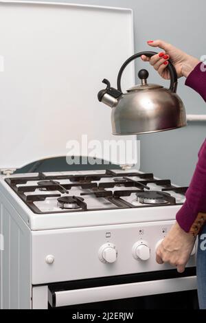 une main femelle place une bouilloire métallique sur un brûleur à gaz. Photo de haute qualité Banque D'Images