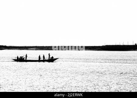 La belle photo en niveaux de gris d'un peuple silhouettes sur un petit bateau traversant le lac Banque D'Images