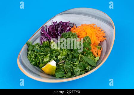 Vue rognée de salade saisonnière de collard verts, verts, carotte râpée de la vue de l'opposé ou de côté, isolée sur fond bleu. Banque D'Images