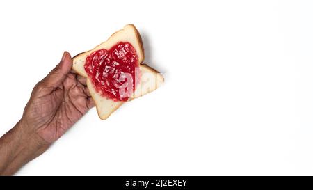 Pain en forme de coeur avec confiture de fruits, tenant le pain à la main, isolé sur fond blanc Banque D'Images