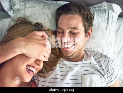 N'arrêtez jamais de faire des souvenirs. Photo d'un jeune homme en jeu couvrant les yeux de ses amies en étant allongé dans le lit. Banque D'Images