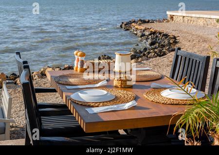 Une table et des chaises en bois avec des plats au café sur la mer attendent les clients. Photo horizontale. Banque D'Images