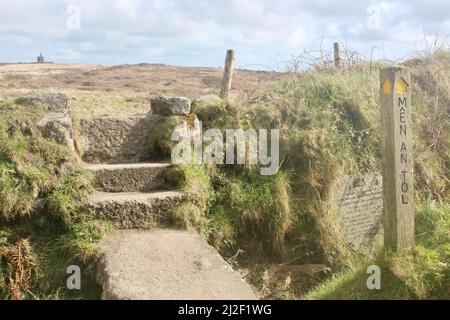 Chemin public porte-affiche à Men an Tol avec un panneau d'information, un stile de pierre et la maison de moteur de mine Ding Dong en arrière-plan. Banque D'Images