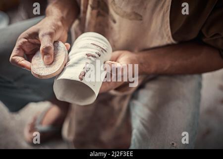 l'artiste lustrant les bords rugueux d'une casserole avec une éponge dans un studio de poterie. Banque D'Images