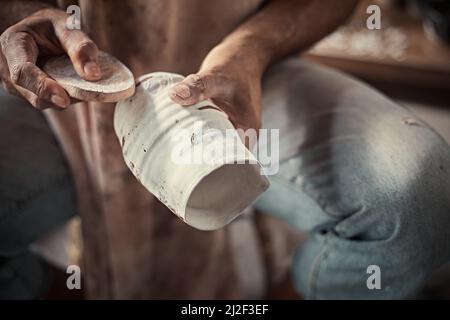 l'artiste lustrant les bords rugueux d'une casserole avec une éponge dans un studio de poterie. Banque D'Images