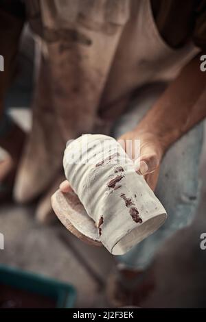 l'artiste lustrant les bords rugueux d'une casserole avec une éponge dans un studio de poterie. Banque D'Images