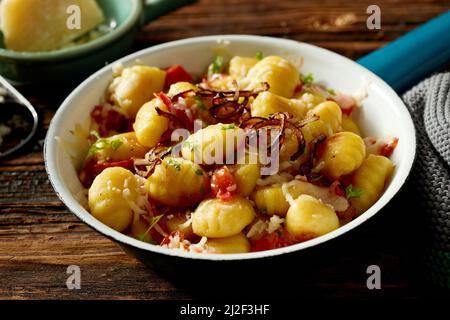 L'appétissant gnocchi de pomme de terre italien traditionnel servi avec un oignon frit aux tomates et du fromage dans un bol sur une table en bois Banque D'Images