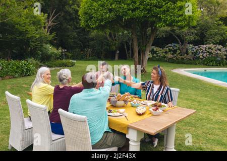 Amis multiraciaux senior, hommes et femmes, qui toasque du vin à table pendant la fête de la cour Banque D'Images