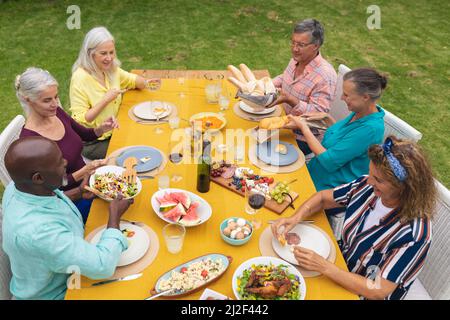 Vue en grand angle des amis séniors multiraciaux appréciant la nourriture à la table pendant la partie arrière-cour Banque D'Images