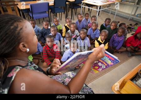 Un bibliothécaire scolaire lit à haute voix un groupe de jeunes enfants dans une classe d'école primaire dans la région d'Oshana, en Namibie, en Afrique australe. Banque D'Images