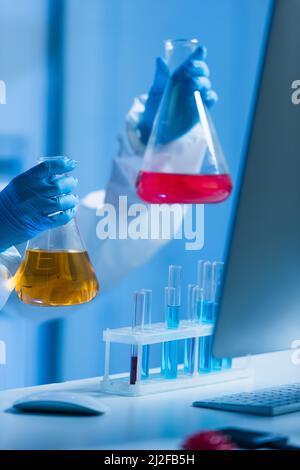 vue rognée des scientifiques tenant une fiole avec un liquide coloré en laboratoire, image de stock Banque D'Images