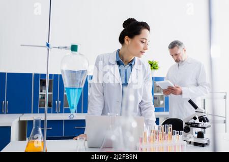 bioingénieur regardant le microscope tout en se tenant près des tubes à essai et des flacons en laboratoire, image de stock Banque D'Images