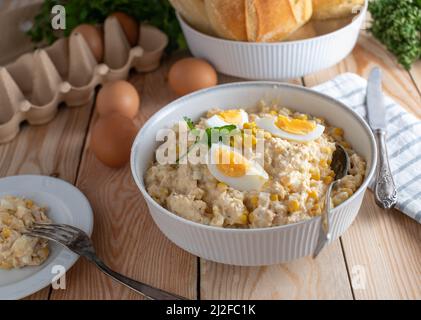 Salade de thon avec mayonnaise, œufs durs, maïs et oignons. Servi dans un bol sur une table en bois Banque D'Images