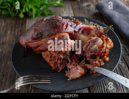 Jarret de porc grillé ou jarret de jambon sur une assiette noire sur fond de table en bois foncé avec vue en coupe transversale. Plat de viande allemand traditionnel Banque D'Images